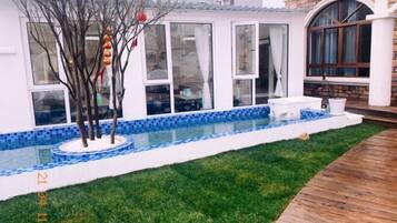 A swimming pool with a tiled edge, a grassy area, and a wooden deck.