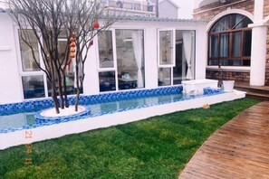 A swimming pool with a tiled edge, a grassy area, and a wooden deck.