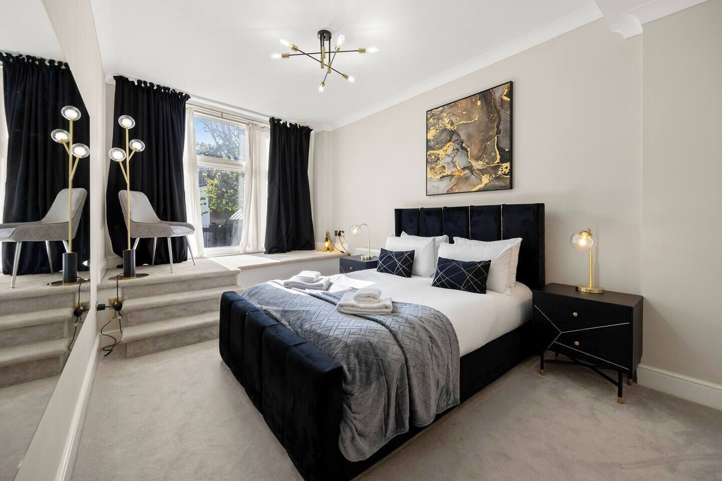 A modern bedroom with a large bed, bedside lamps, a window with curtains, and a painting on the wall.