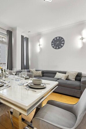 Ein stilvoller Essbereich mit einem Tisch für vier Personen, einem grauen Sofa und einer Wanduhr.