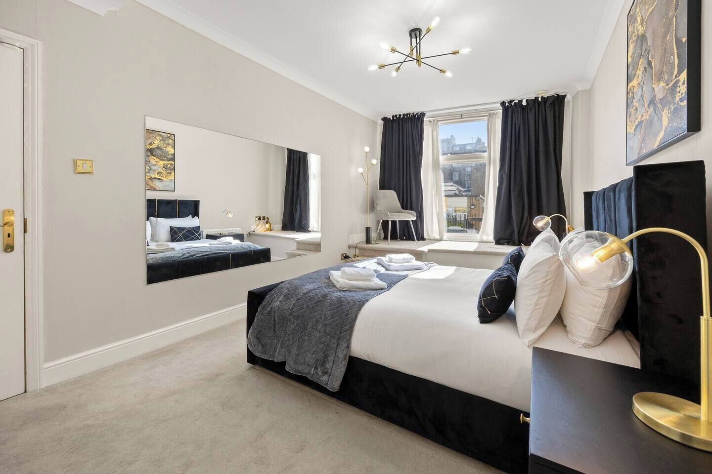 A modern bedroom with a large bed, a mirror, a desk, and a chair.