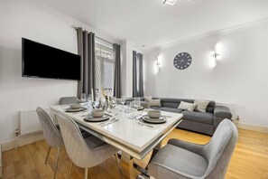 Ein modernes Wohnzimmer mit Essbereich, einem grauen Sofa, einem Flachbildfernseher und einer Wanduhr.