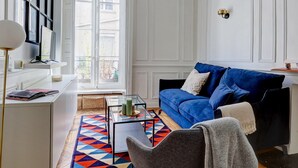 A modern living room with a blue sofa, a glass coffee table, and a patterned rug. - Stylish 1BR in the Heart of Le Marais (Paris)