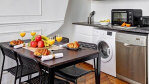 A modern kitchen with white cabinetry, a built-in oven, microwave, and dishwasher. There is a dining table with chairs and a breakfast setting. - Stylish 1BR in the Heart of Le Marais (Paris)