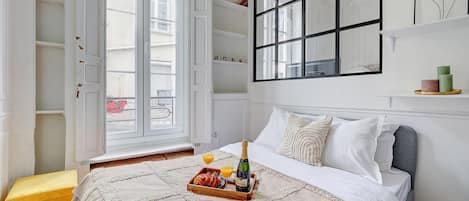 Um quarto com uma cama, uma janela, uma estante de livros e uma revista sobre a cama.