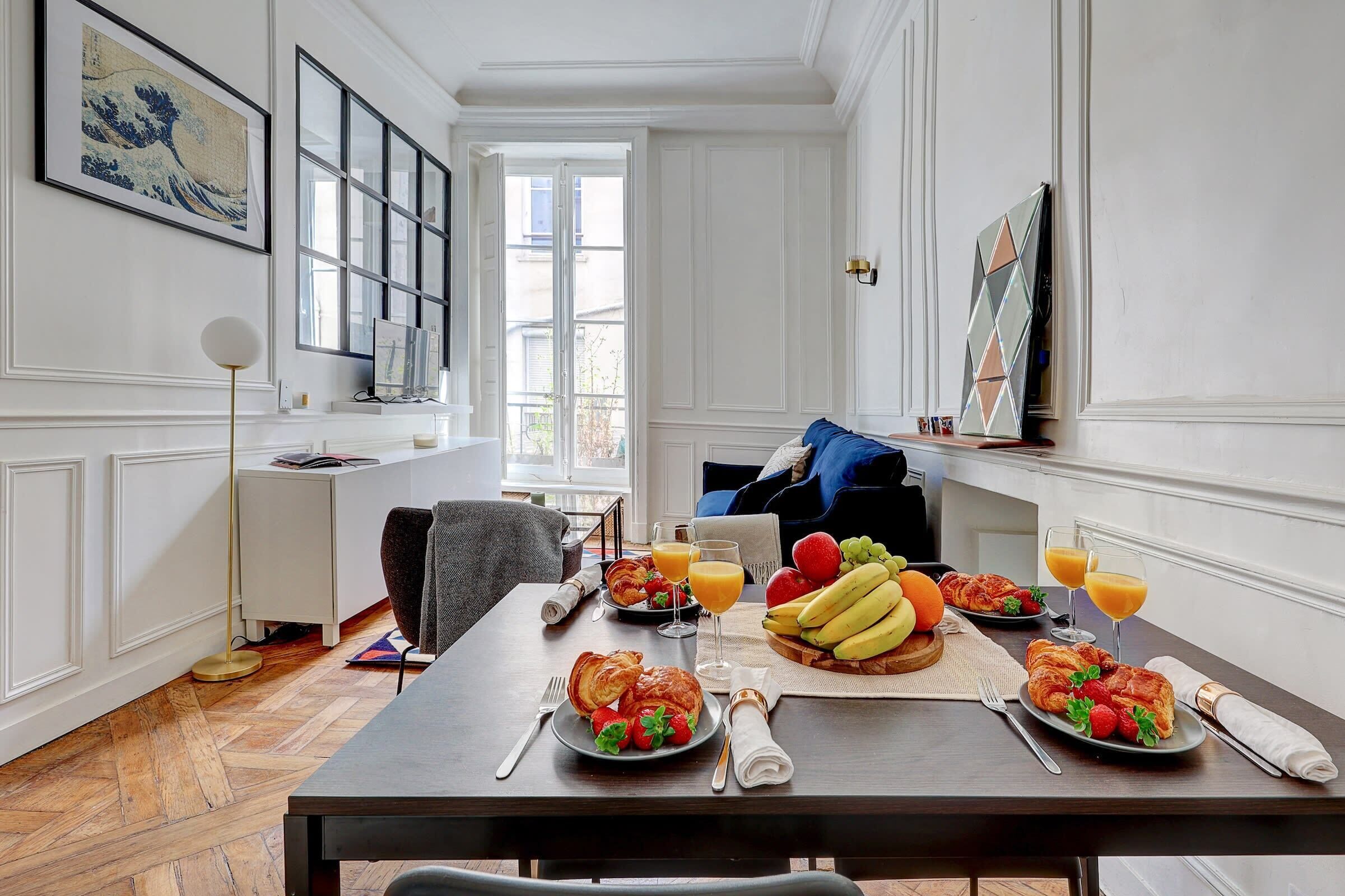 A dining area with a wooden table set for breakfast, a sofa, and a large window with a view.