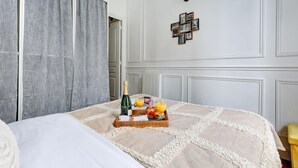A hotel room with a bed, a tray with breakfast items, and a wall with framed pictures. - Stylish 1BR in the Heart of Le Marais (Paris)