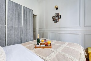 A hotel room with a bed, a tray with breakfast items, and a wall with framed pictures. - Stylish 1BR in the Heart of Le Marais (Paris)