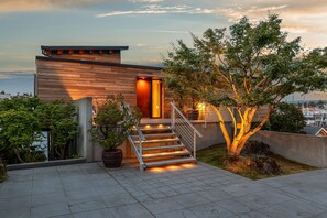 Une maison moderne avec une façade en bois, un escalier doté de rampes en métal et un arbre au premier plan.