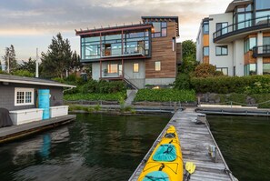 A modern waterfront property with a dock, a yellow kayak, and a building with large windows and a wooden facade. - Stunning Waterfront! Tom Kundig-Designed, Dock, Fire Pit & Bay Views (Seattle)