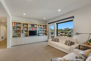 A spacious living room with a large bookshelf, a flat-screen TV, and a sofa. - Stunning Waterfront! Tom Kundig-Designed, Dock, Fire Pit & Bay Views (Seattle)