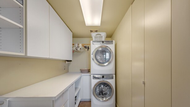 A laundry room with two stacked front-loading washing machines, a drying machine, and a white countertop with a basket. - Stunning Waterfront! Tom Kundig-Designed, Dock, Fire Pit & Bay Views (Seattle)