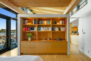 A modern library with wooden bookshelves, a desk, and a view of a marina through large windows. - Stunning Waterfront! Tom Kundig-Designed, Dock, Fire Pit & Bay Views (Seattle)