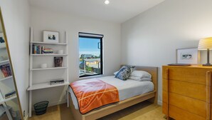 A bedroom with a bed, a window with a city view, a bookshelf, and a wooden dresser. - Stunning Waterfront! Tom Kundig-Designed, Dock, Fire Pit & Bay Views (Seattle)