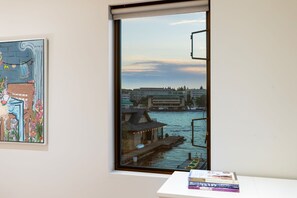 Ein Zimmer mit Fensterblick auf das Wasser, ein gerahmtes Bild an der Wand und Bücher auf einem Tisch.
