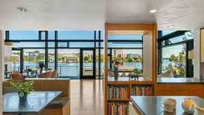 A modern kitchen with a view of a waterfront, wooden cabinets, and a bookshelf with books. - Stunning Waterfront! Tom Kundig-Designed, Dock, Fire Pit & Bay Views (Seattle)