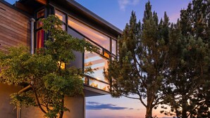 A modern building with large windows and a balcony overlooking a forested area. - Stunning Waterfront! Tom Kundig-Designed, Dock, Fire Pit & Bay Views (Seattle)