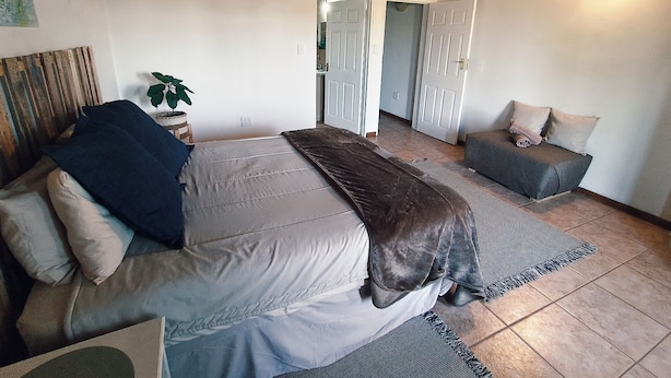 A bedroom with a bed, a sofa, a plant, and a ceiling with wooden beams. - Lemon & Co (Bela-Bela)