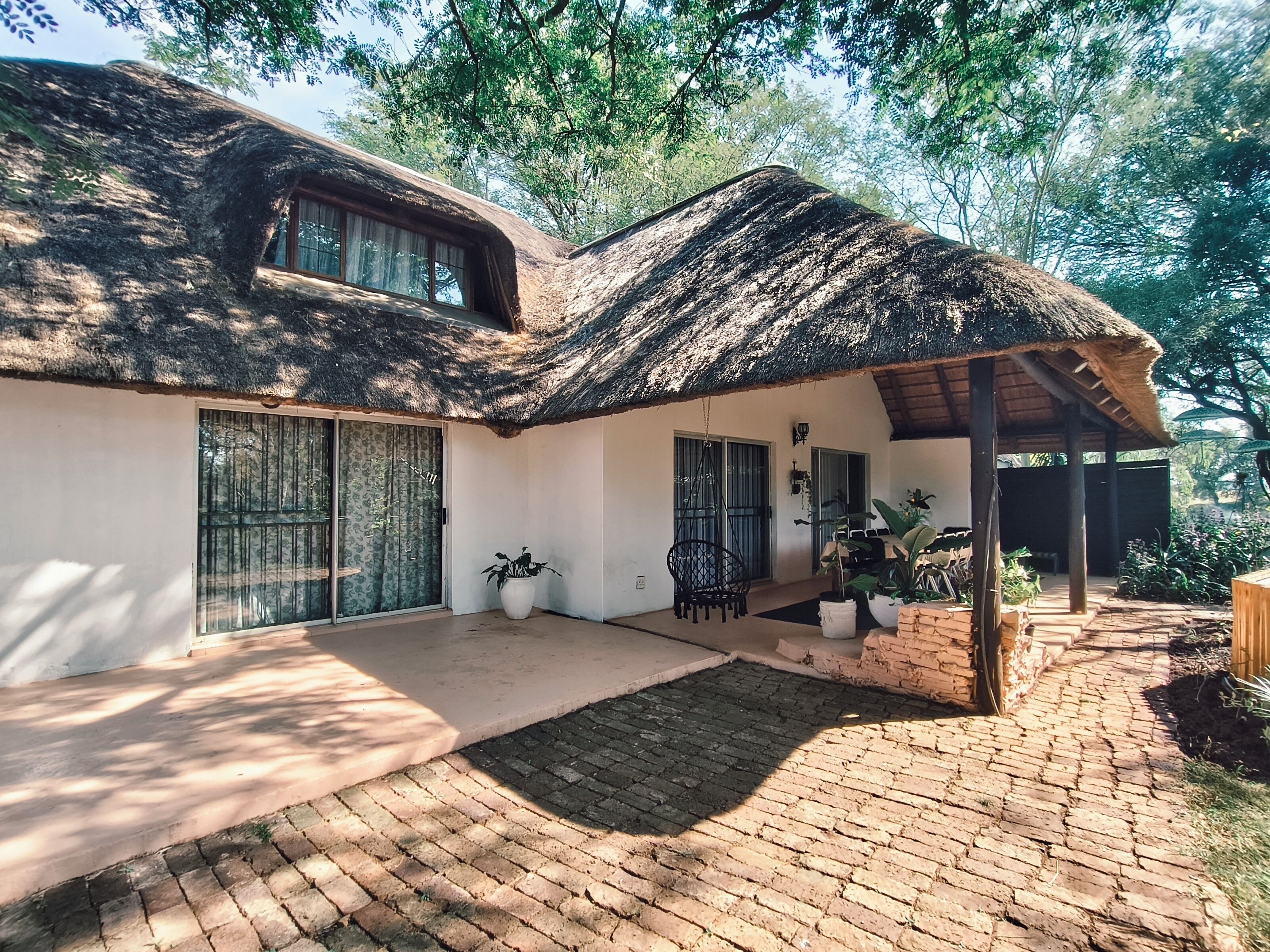 A house with a thatched roof, large windows, and a paved courtyard.