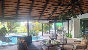 A covered outdoor seating area with a pool, lounge chairs, and potted plants. - Lemon & Co (Bela-Bela)