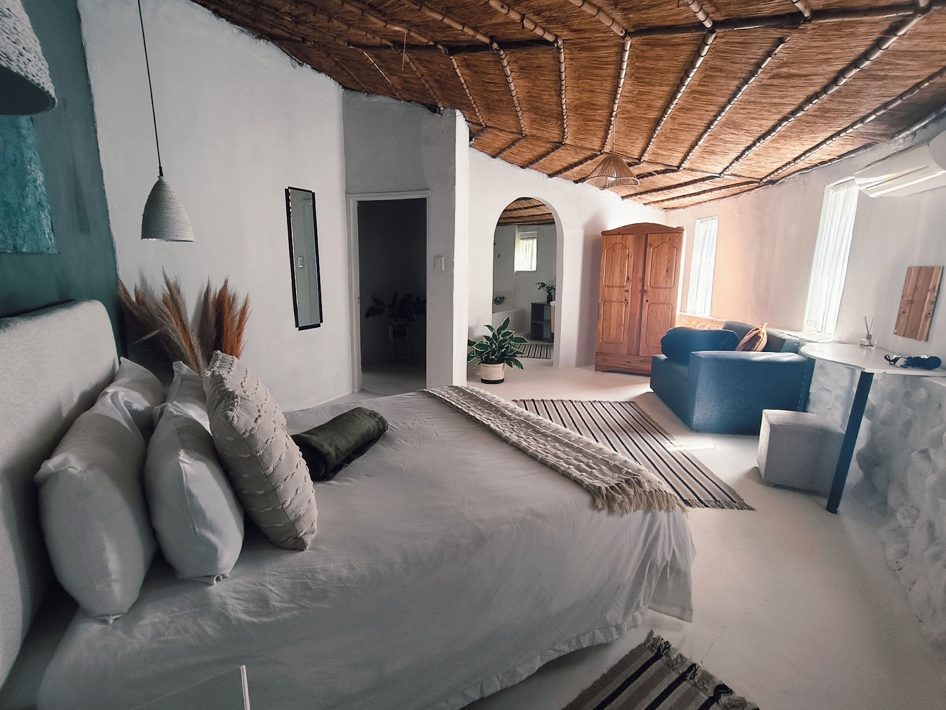 A bedroom with a bed, a blue sofa, a wooden wardrobe, and a hanging light fixture.