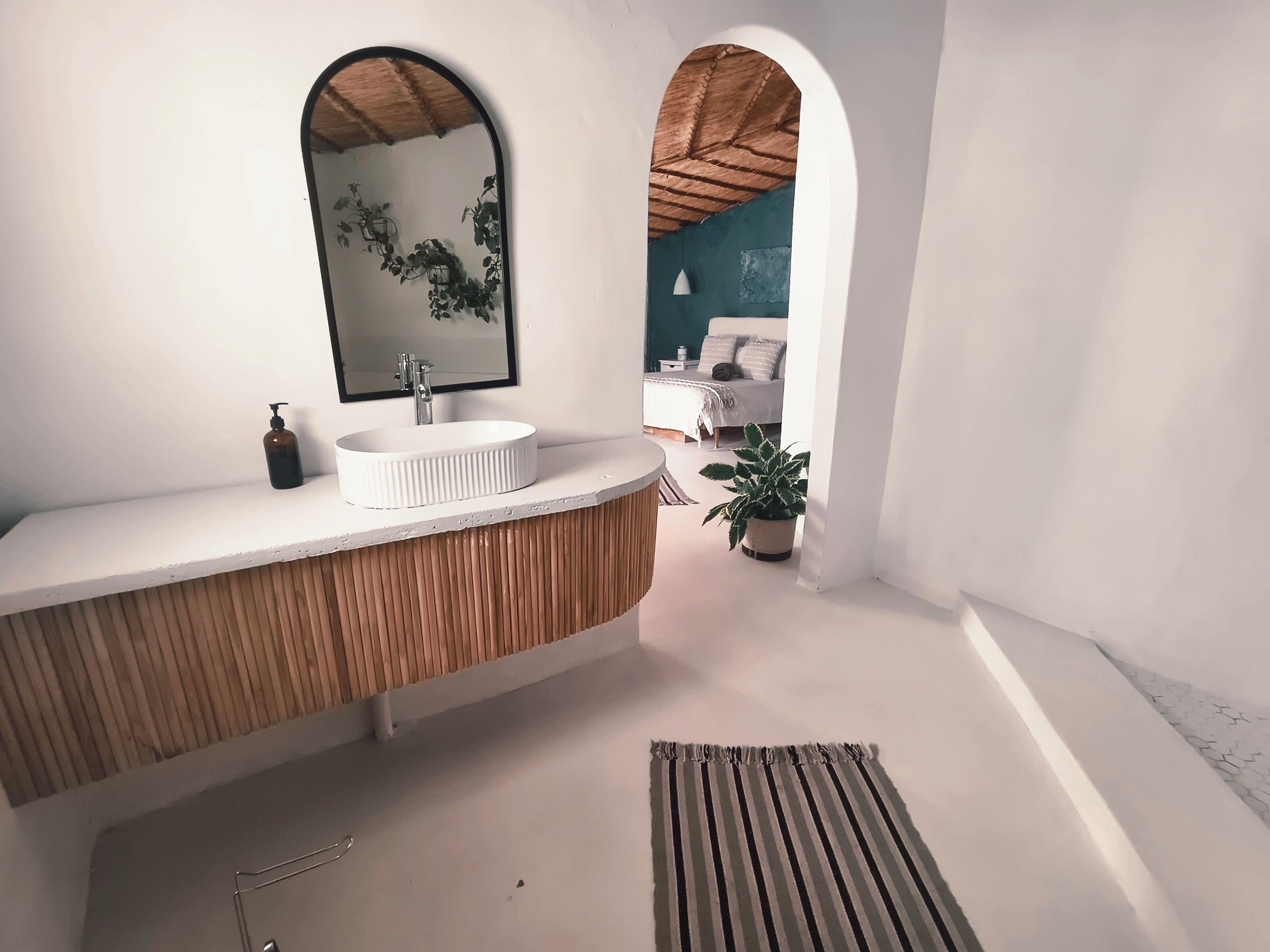 Een moderne badkamer met een witte wastafel, een grote spiegel en een plant in pot.