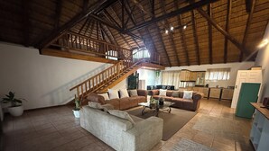 A spacious living area with a high ceiling, a staircase, and a kitchen area. - Lemon & Co (Bela-Bela)