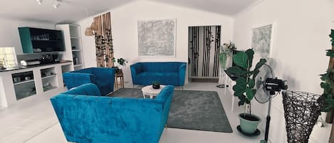 A modern living room with blue sofas, a coffee table, a TV, and a large plant.