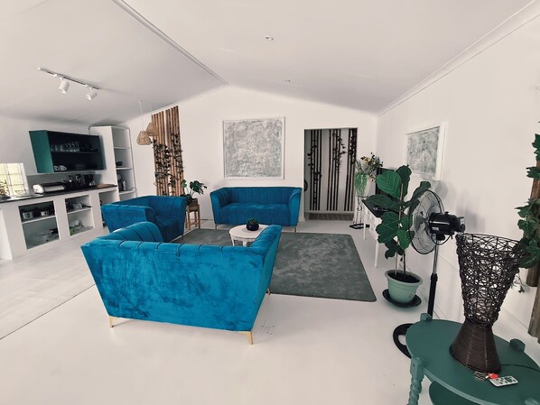 A modern living room with blue sofas, a coffee table, a TV, and a large plant.