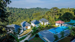 Un resort con varias villas, una piscina y abundante vegetación al fondo.