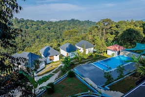 A resort with multiple villas, a swimming pool, and lush greenery in the background.