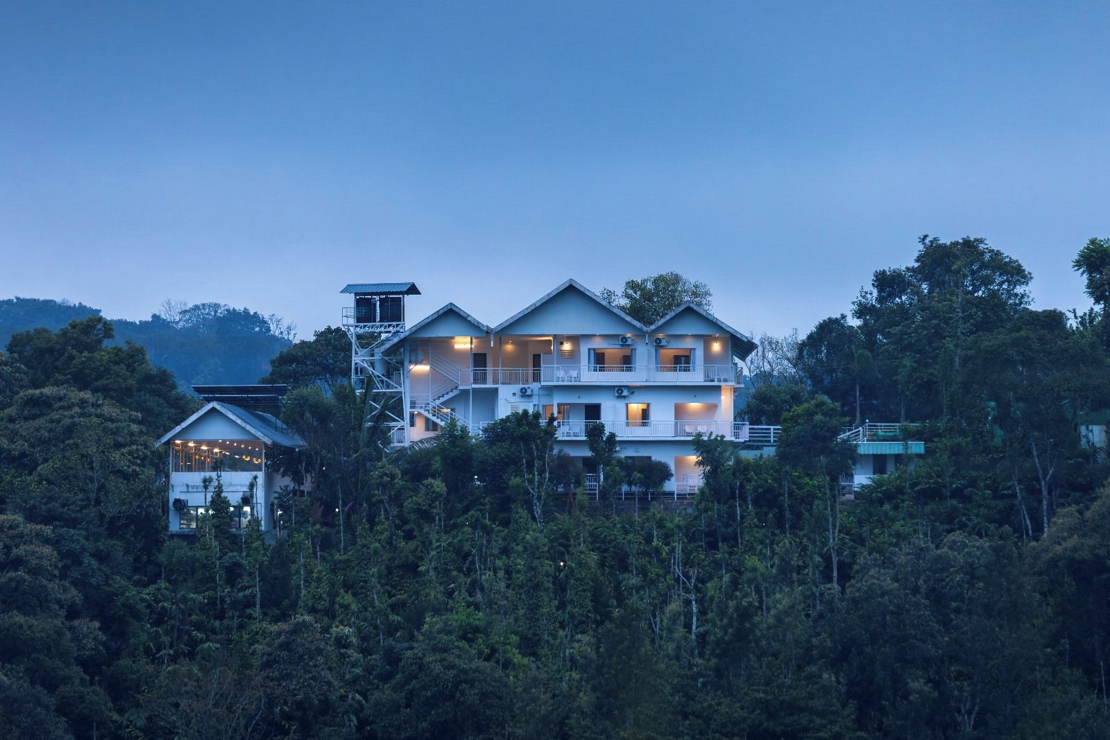 Um edifício com várias andares e varandas, rodeado por uma floresta densa.