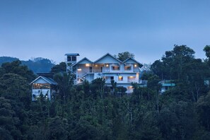 Un edificio de varios pisos con balcones, rodeado de un bosque frondoso.