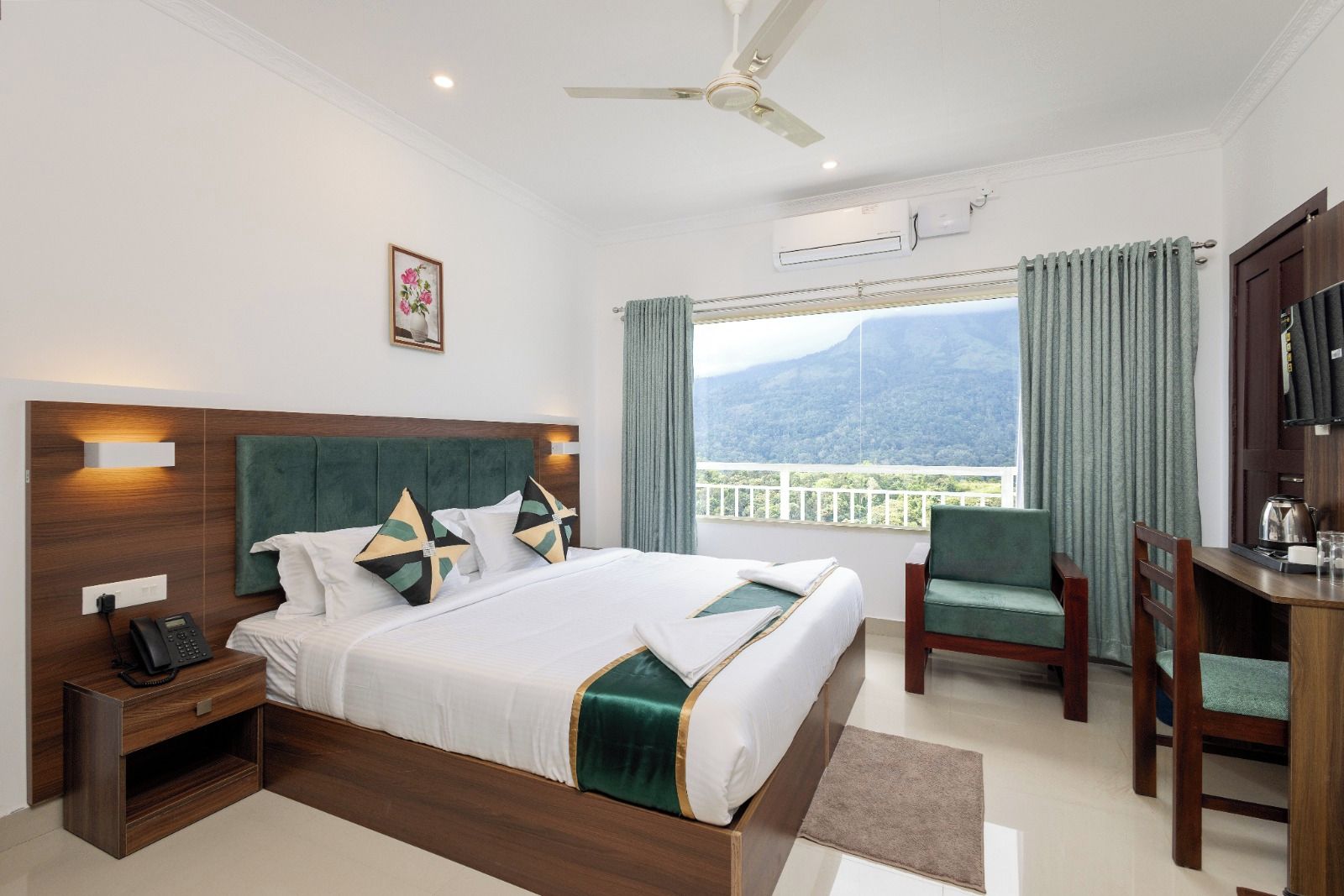 A hotel room with a bed, a desk, a chair, a phone, and a view of the mountains.