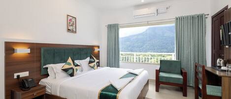 A hotel room with a bed, a desk, a chair, a phone, and a view of the mountains.