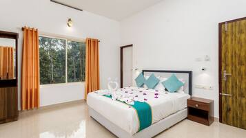 Quarto de hotel com uma cama grande, um guarda-roupa de madeira, uma mesa de cabeceira e uma janela com cortinas.