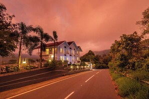 Un hôtel à plusieurs étages doté d’un balcon au deuxième étage, d’une entrée bien éclairée et d’une route menant à l’établissement.