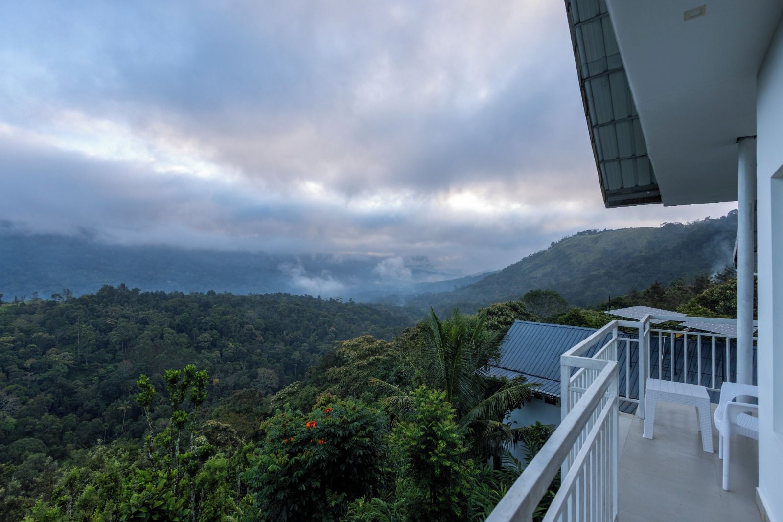Varanda com vista para uma cadeia montanhosa arborizada e céu nublado.