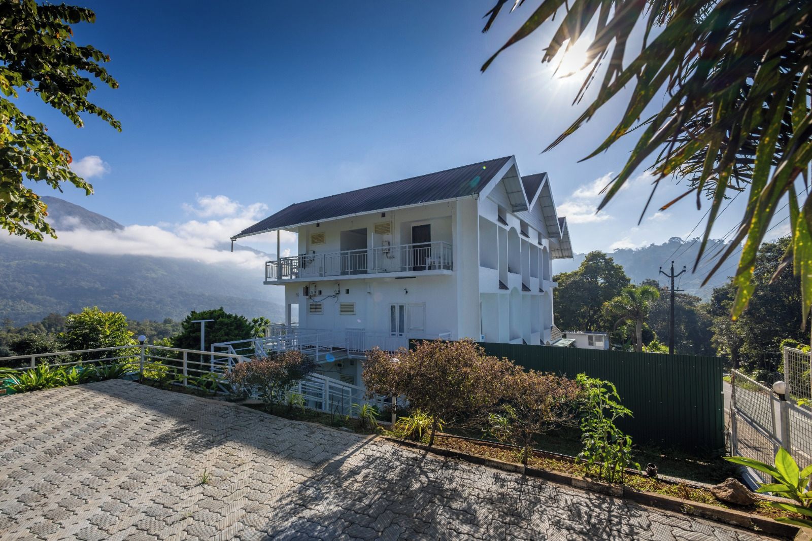 A two-story building with a balcony, surrounded by greenery and a mountainous backdrop.