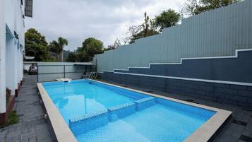 Una piscina rectangular con borde de azulejos, rodeada por un sendero empedrado y un muro bajo.