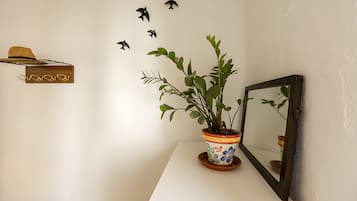 Una pared blanca con una planta en maceta, un espejo y un sombrero en un estante.