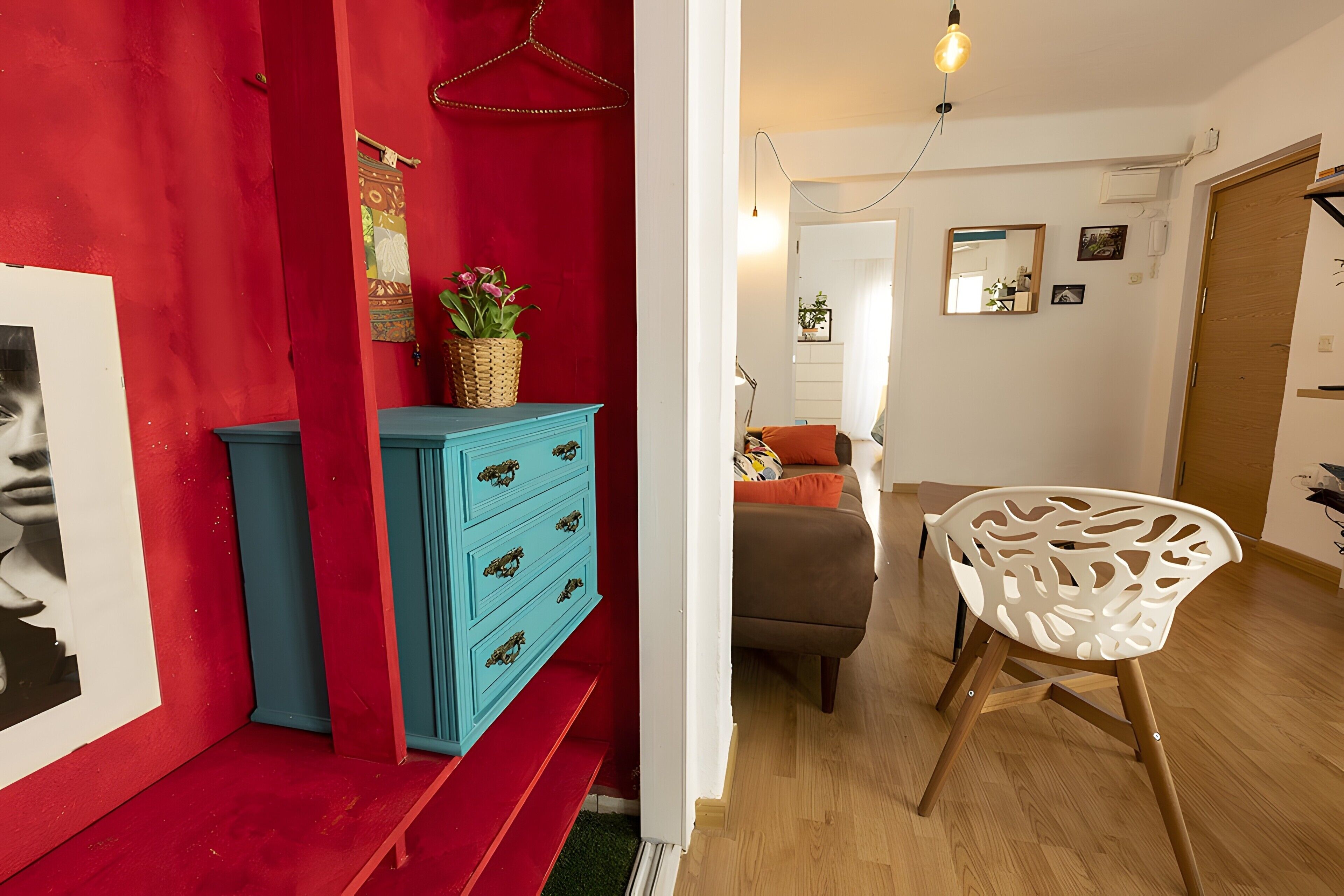 Ein Zimmer mit roter Wand, einem blauen Schminktisch, einem weißen Stuhl und einem braunen Sofa.