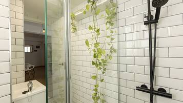 Un baño moderno con paredes de azulejos blancos, cabina de ducha de vidrio, ducha de mano y una planta en maceta.