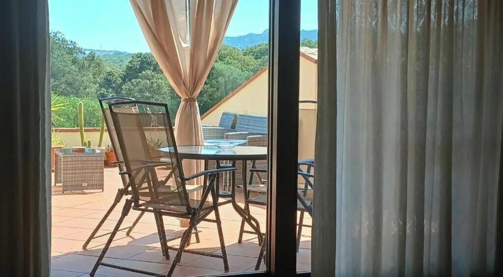Un patio exterior con mesa y sillas, vistas a zonas verdes y un edificio al fondo.