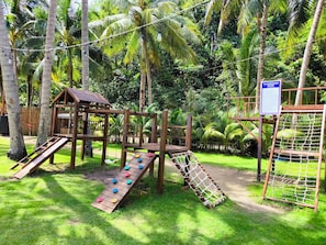 A playground with a wooden slide, climbing net, and a small house structure.