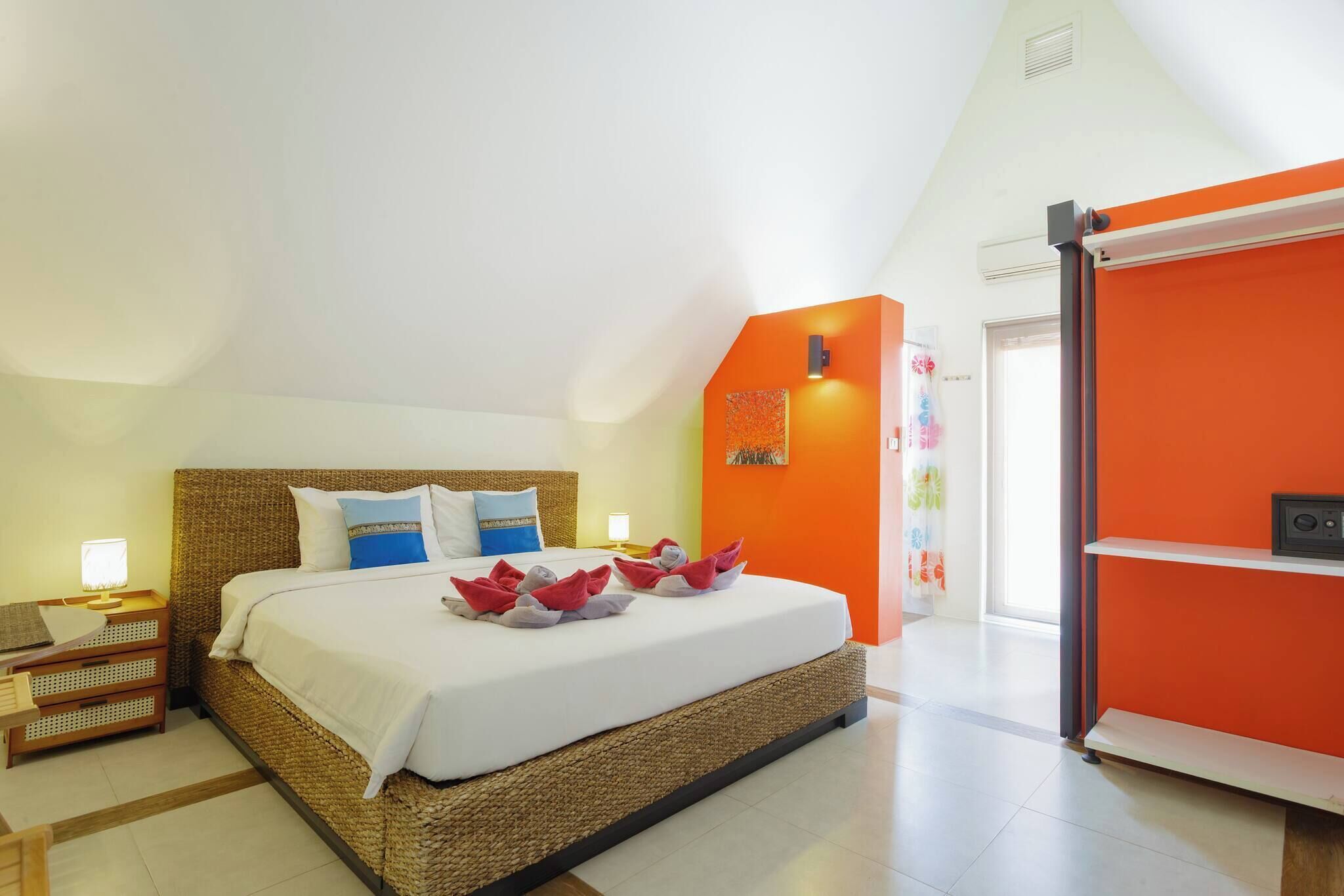 A hotel room with a bed, a nightstand, a lamp, and a bright orange accent wall.
