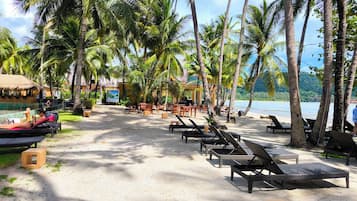 Resort à beira-mar com espreguiçadeiras, piscina e palmeiras.