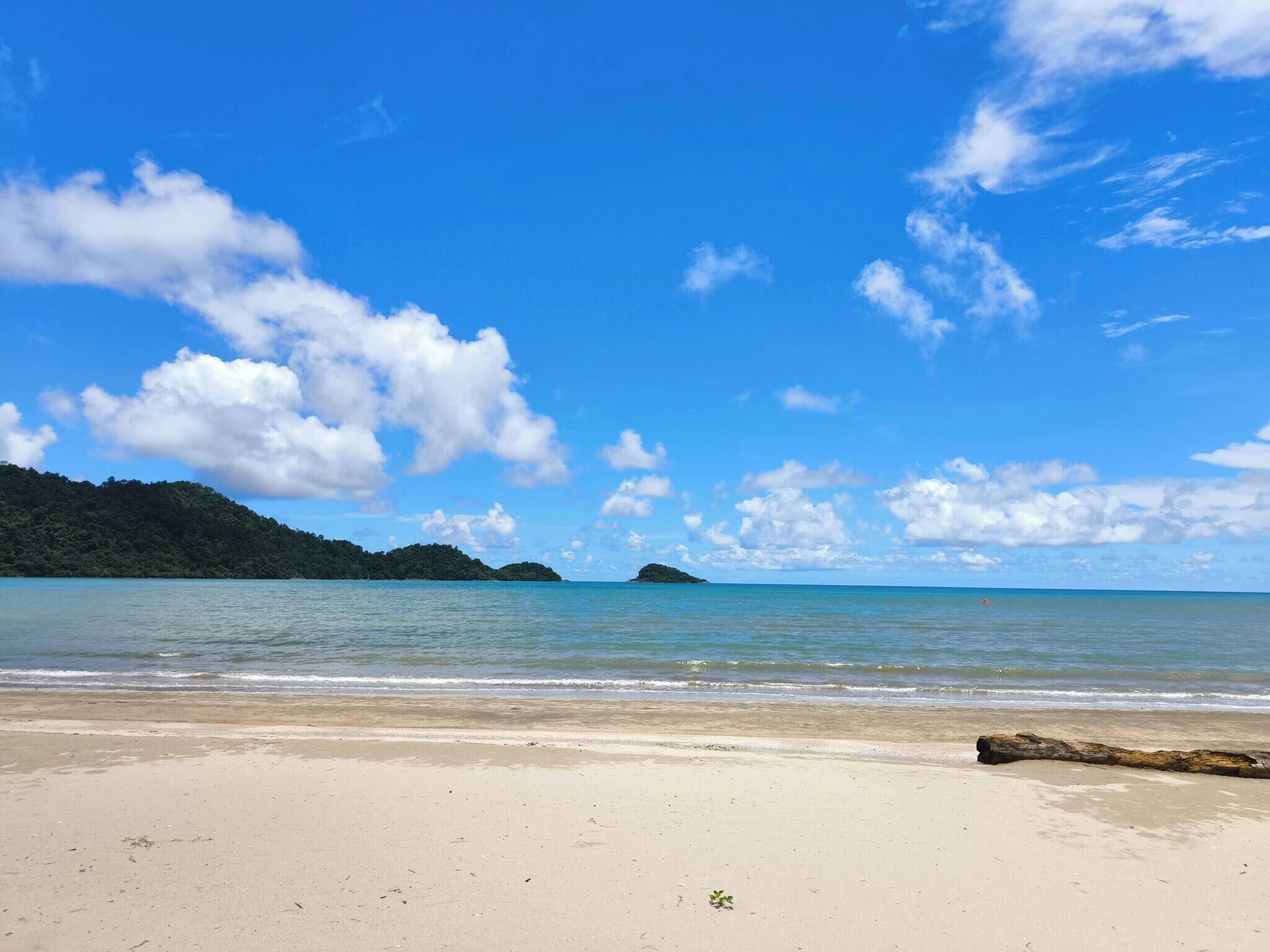 A beach with clear skies, calm water, and distant islands.