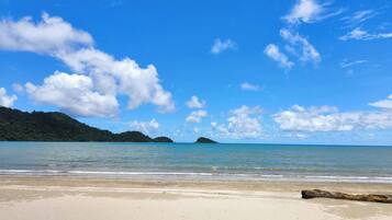 A beach with clear skies, calm water, and distant islands.