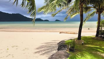 Uma praia com águas turquesa cristalinas, palmeiras e uma grande formação rochosa.